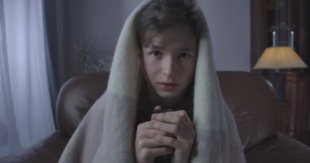 Portrait of scared teenager watching horror movie at night. Close-up of frightened brunette Caucasian boy wrapped in blanket moving back from TV. Fear, anxiety, lifestyle. Cinema 4k ProRes HQ. - Кадри, відео