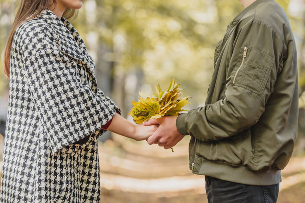 Autumn concept. Bouquet of bright colorful autumn leaves in hands of two people in love against blurred park background. - Foto, Imagem