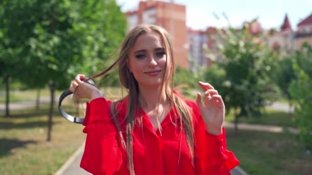 Beautiful girl with headphones walking in the city. Young woman with long hair listening to music through the headphones outdoors. Slow motion. - Footage, Video