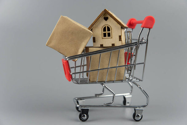 Buying a house, building repair and mortgage concept. Estimation real estate property with loan money and banking. House in shopping cart on grey background. - Photo, Image