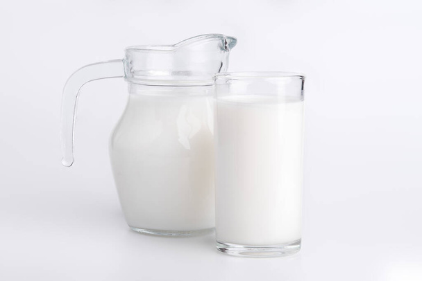 Természetes teljes tej egy kancsóban és egy üveg fehér háttérrel. tej stand egy tiszta fehér háttér. - Fotó, kép