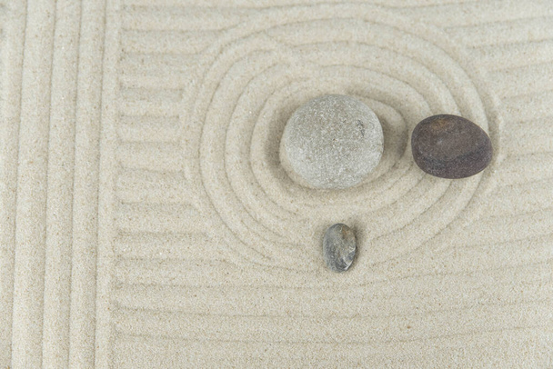 Κήπος Ζεν. Πυραμίδες από άσπρες και γκρι ζεν πέτρες στη λευκή άμμο με αφηρημένα κυματικά σχέδια. Έννοια της αρμονίας, της ισορροπίας και του διαλογισμού, spa, μασάζ, χαλάρωση. - Φωτογραφία, εικόνα
