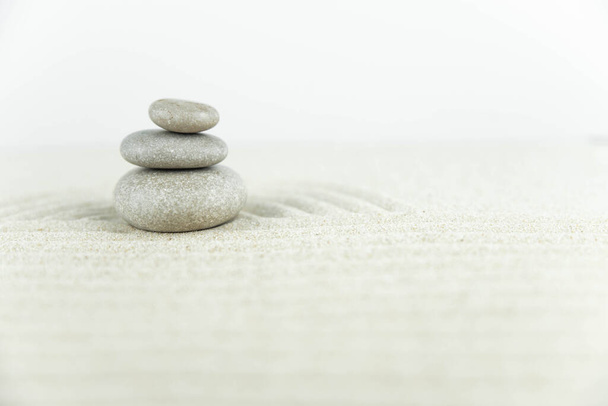 Zen-Garten. Pyramiden aus weißen und grauen Zen-Steinen auf dem weißen Sand mit abstrakten Wellenzeichnungen. Konzept der Harmonie, Balance und Meditation, Wellness, Massage, Entspannung. - Foto, Bild