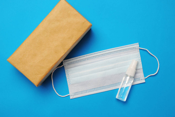 Bruin gesloten kartonnen verpakkingsdoos, handreiniger spray en chirurgisch gezichtsmasker als bescherming tegen influenza - Foto, afbeelding