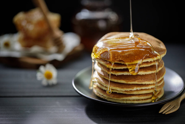 木製のテーブルの上で朝食のためのパンケーキのスタックにドリンピング蜂蜜、有機天然成分による健康的な製品が含まれています - 写真・画像