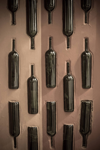 Wall, vertical surface, decorated with empty, glass, wine bottles. Bar, pub, alcohol shop. Daytime side lighting. Vertical arrangement. - Photo, Image