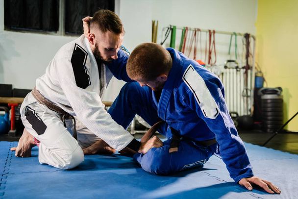 Brazilský Jiu Jitsu BJJ bojová umění trénink sparring na akademii dva bojovníci v pozici motýla stráž vrtné techniky cvičení v gi kimono - Fotografie, Obrázek