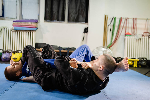 Braziliaanse Jiu jitsu BJJ jiujitsu training sparring atleet vechter toepassen arm bar armbar indiening op zijn tegenstander techniek praktijk dragen kimono gi - Foto, afbeelding