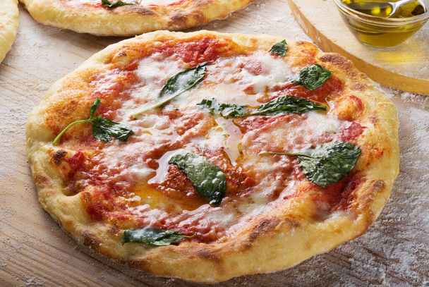 Pizza Margherita fraîchement cuite sur une planche à pâtisserie farinée en bois, gros plan
. - Photo, image