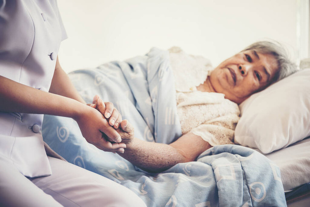 Nahaufnahme einer jungen Krankenschwester, die sich um ältere Patienten kümmert, die sie halten und dafür sorgt, dass sie sich während der Aufnahme im Krankenhaus wohlfühlt. - Foto, Bild