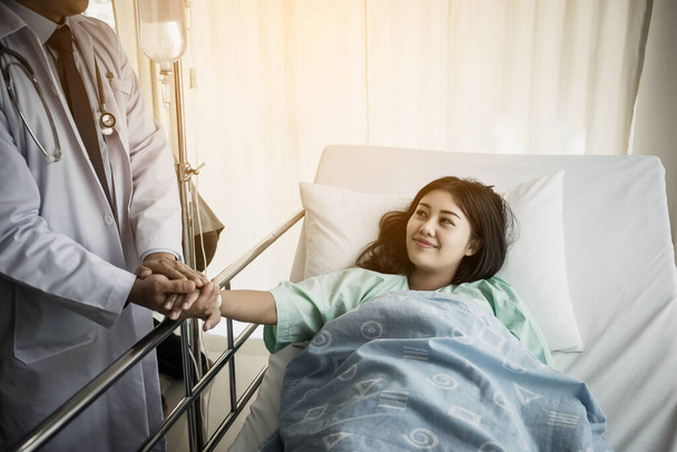 Een arts die met een patiënt praat en haar hand vasthoudt om haar te troosten. Vrouwelijke patiënt met letsel liggend op bed in het ziekenhuis. - Foto, afbeelding