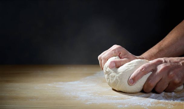 The baker`s hands kneading bread or pizza dough on a wooden pastry board, space for text. - Φωτογραφία, εικόνα