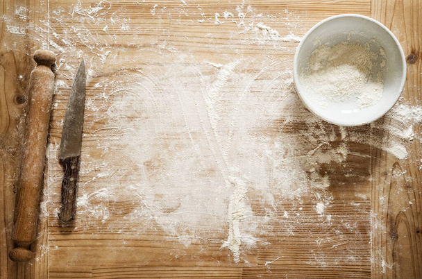 Pastry board with knife, flour and rolling pin, top view, space for text. Flour in a bowl on floured wooden background. - Photo, Image