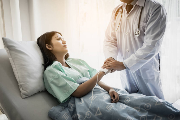 Een arts die met een patiënt praat en haar hand vasthoudt om haar te troosten. Vrouwelijke patiënt met letsel liggend op bed in het ziekenhuis. - Foto, afbeelding