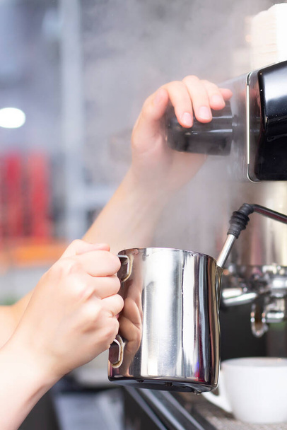 Coffee shop worker preparing coffee on steam espresso coffee machine. Barista Warming Milk In Metal Jug With Steam Of Coffee Machine. vertical photo - Foto, Bild