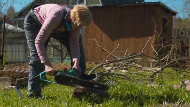 Mature woman cutting tree with an electric saw - Footage, Video