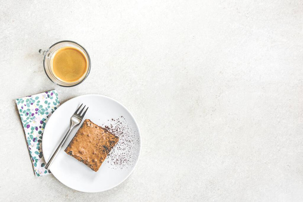 Top view of a cup of coffee and a dessert plate with brownie cake over white rustic background. - Photo, Image