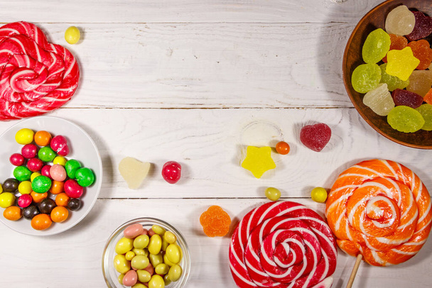 Kolorowe czekoladowe cukierki, lizaki i galaretki na białym drewnianym stole - Zdjęcie, obraz