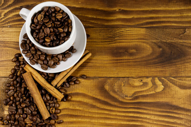 Coffee beans in white cup and cinnamon sticks on wooden table. Top view, copy space - 写真・画像