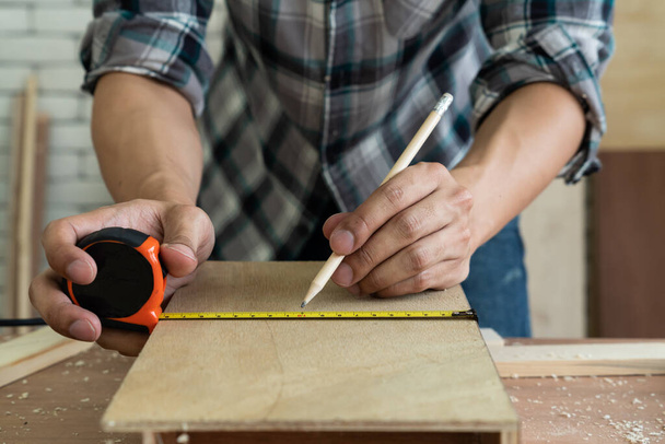 Tischler, der in einer Werkstatt mit Holzhandwerk beschäftigt ist, um Baumaterial oder Holzmöbel herzustellen. Der junge asiatische Tischler setzt professionelle Werkzeuge zum Basteln ein. Heimwerker und Zimmerer arbeiten Konzept. - Foto, Bild
