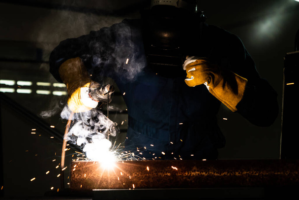 Metal welder working with arc welding machine to weld steel at factory while wearing safety equipment. Metalwork manufacturing and construction maintenance service by manual skill labor concept. - Φωτογραφία, εικόνα