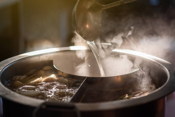 Cooking person in the restaurant is cooking while using the dipper in a large soup pot. And the water is boiling, there is smoke and hot spit. - Foto, imagen
