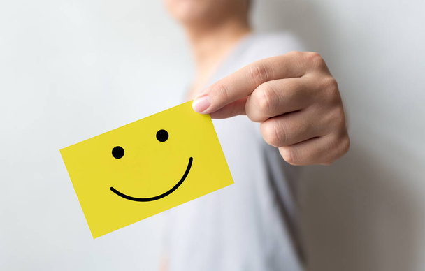 Customer service experience and business satisfaction survey. Man holding yellow card with smiley face - Photo, Image