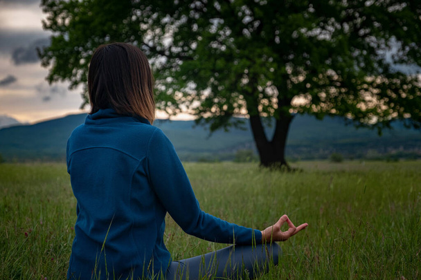Eine junge Frau macht Yoga in der Nähe einer einsamen Eiche bei Sonnenuntergang in der Natur. Selbstanalyse und Gewissenserforschung. Spirituelles und emotionales Konzept. Selbstbetrachtung und Seelenheilung. zurück - Foto, Bild