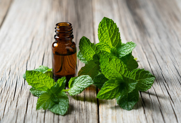 An essential oil bottle set against an old wooden backdrop. Mint leaves around. - Photo, Image