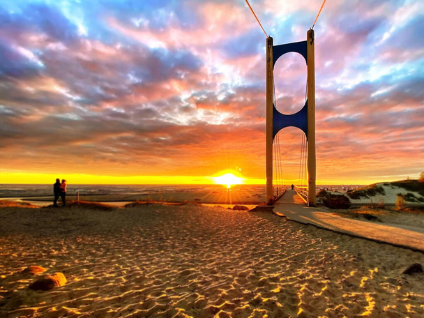 όμορφο ηλιοβασίλεμα στη θαλάσσια πύλη γέφυρα στον ήλιο φως παραλία άνθρωποι περπάτημα ρομαντικό ζευγάρι διαμονή στην άμμο αντανάκλαση στο θαλάσσιο κύμα ρομαντικό συννεφιασμένο ουρανό φόντο φύση τοπίο  - Φωτογραφία, εικόνα