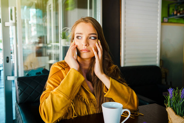 Portret van een jonge mooie vrouw in café restaurant die met het mobiele telefoongesprek praat en verontrustend verrassend nieuws ontvangt. - Foto, afbeelding