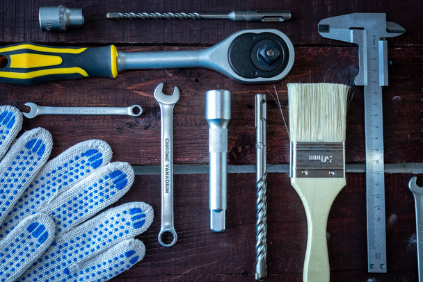 Construction tools are laid out on a wooden background. Spanners, brushes, calipers, gloves - Photo, Image