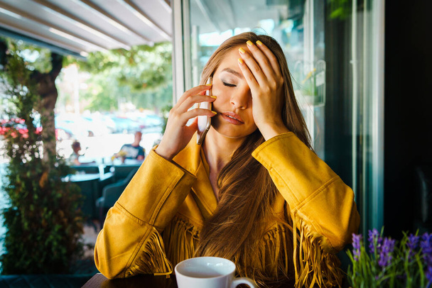 Портрет молодої красивої жінки в кафе ресторан розмовляє з мобільним телефоном, отримуючи тривожні новини, що тримають голову ручним чолом
 - Фото, зображення
