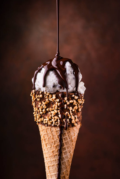 Конус мороженого с каплями расплавленного темного шоколада и рубленых лесных орехов
 - Фото, изображение