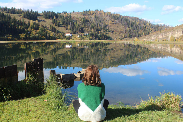 Young woman in a green sweater sits near the lake in autumn - Foto, Bild