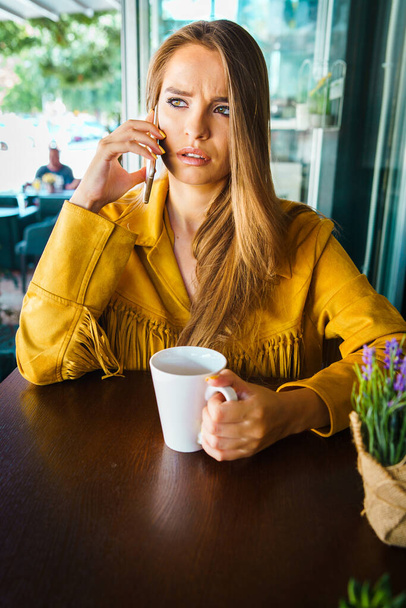 Retrato de una joven hermosa mujer en el restaurante cafetería hablando con la llamada de teléfono móvil recibiendo inquietantes noticias sorprendentes cara reaccionando
 - Foto, imagen