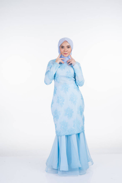 Aantrekkelijk moslim vrouwelijk model met pastelblauw moderne kurung met hijab, een urban lifestyle kleding voor moslimvrouwen geïsoleerd op witte achtergrond. Schoonheid en hijab mode concept. Totale lengte - Foto, afbeelding