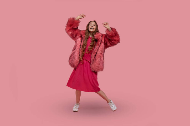girl in a fashionable fur coat with fur, a pink dress and gym shoes is dancing - Foto, Imagen