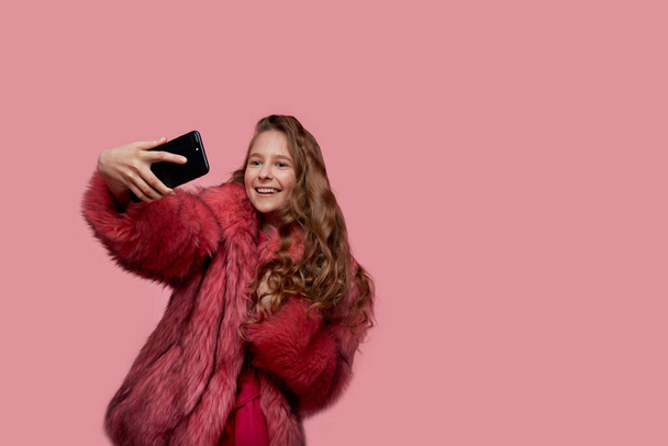 Beautiful young girl in a fashionable pink fur coat. The phones in hand. - Foto, Imagen