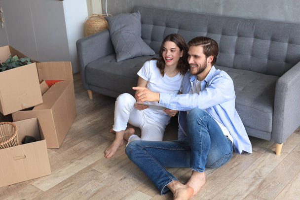 Happy couple sitting and planning new home decoration at home with a tablet at moving day, renovation and interior design for new house. - Photo, Image