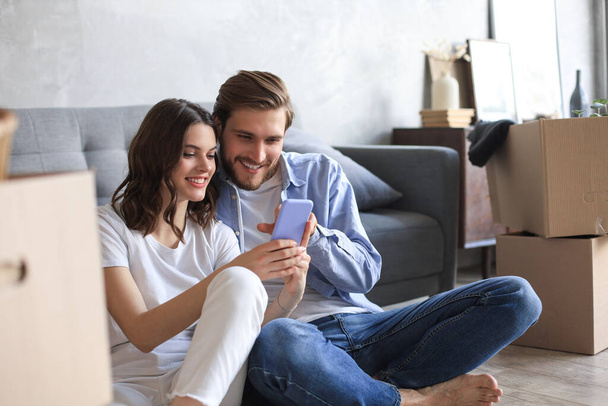 Happy couple sitting and planning new home decoration at home with a smartphone at moving day, renovation and interior design for new house. - Foto, immagini