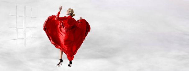 Красива і сексуальна жінка у червоній сукні стоїть перед вікном на хмарах у День святого Валентина. - Фото, зображення