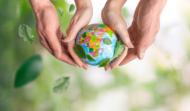 Male and female hands holding the earth on a background of green leaves and spring summer background. Save planet, economical consumption, eco, ecology. Symbolic of peaceful and safe the Earth. - Photo, Image