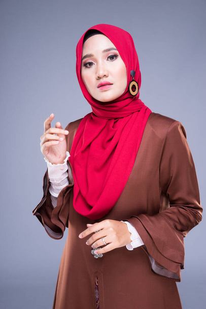 Retrato de media longitud de una hermosa modelo femenina con un vestido de kebaya moderno y hijab, una ropa de estilo de vida para mujeres musulmanas aisladas sobre fondo gris. Belleza y hijab concepto de moda
. - Foto, imagen