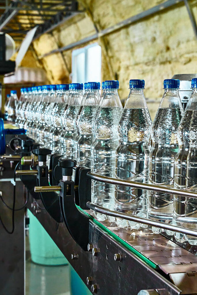 Pure drinking water plant. Work conveyor in the enterprise. Liter bottles on the conveyor are filled with water - 写真・画像