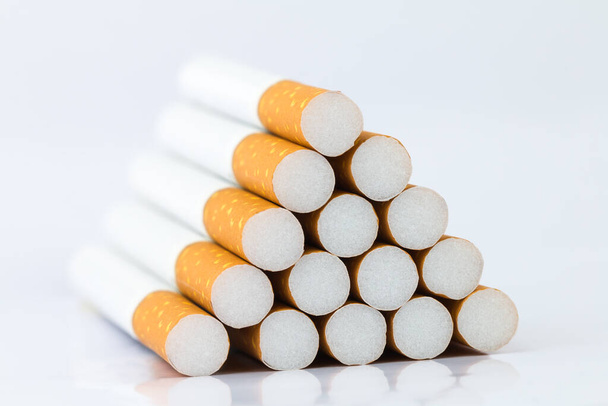 Monien savukkeiden lähikuva Savukkeen pää on ruskea ja kärki valkoinen. Järjestetty kolmio valkoisella pohjalla - Valokuva, kuva