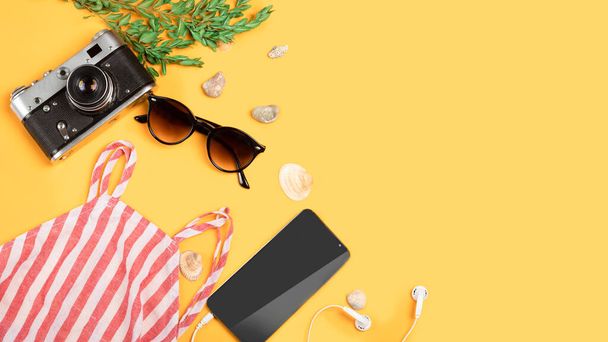 Yellow summer background with sunglasses, a vintage camera, a female top, sea shells, a phone with headphones. Flat lay with copy space. Summer holiday, travel concept. - Photo, Image