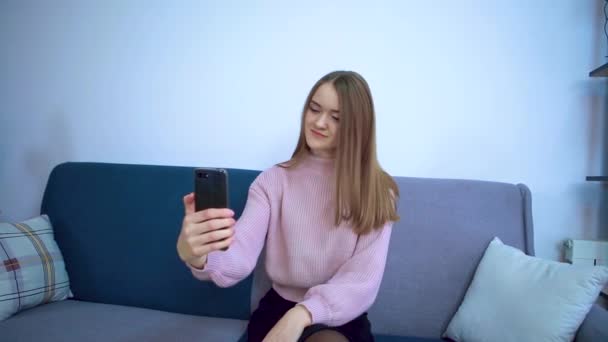 Uma menina em um quarto grande senta-se em um sofá fotografa-se no telefone
. - Filmagem, Vídeo