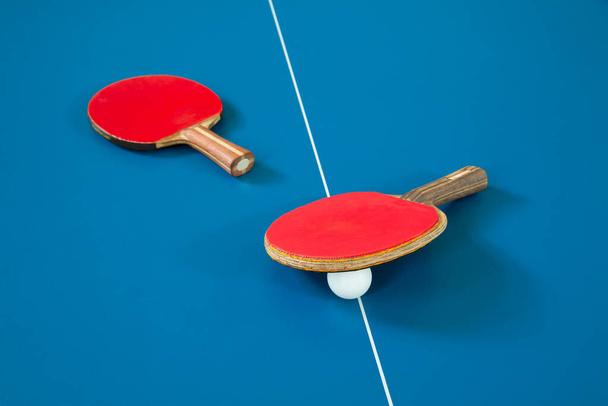 Raquetas para tenis de mesa de color rojo y una pelota sobre una mesa de tenis
 - Foto, imagen