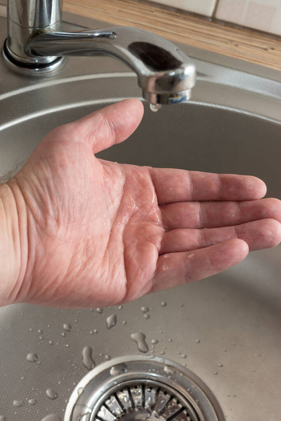 Σταγόνες νερού στάζουν σε παλάμη mans που ελέγχει αν υπάρχει νερό στη βρύση κουζίνα - Φωτογραφία, εικόνα
